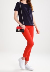 Mörkblå kortärmad topp med samlad halsringning, matchad med figurnära röda byxor. Accessoarer inkluderar en svart och röd axelväska och vita sneakers.