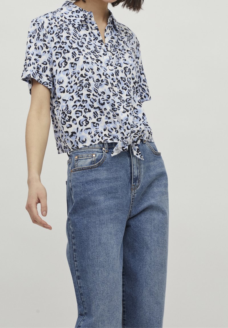 Blusa a maniche corte, di colore azzurro, con stampa leopardata, legata in vita, abbinata a jeans in denim blu a vita alta. Tessuto morbido e vestibilità rilassata.