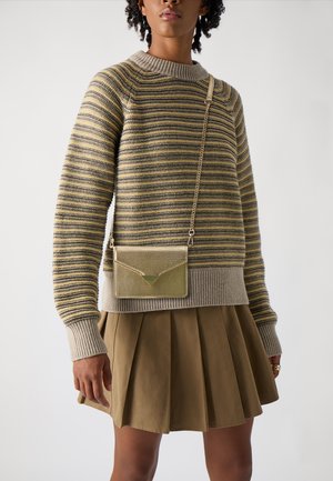 Sweter w poziome paski w kolorze beżowym, oliwkowym i szarym, z prążkowanym kołnierzem. Połączony z brązową spódnicą plisowaną i metaliczną złotą torebką na ramię.