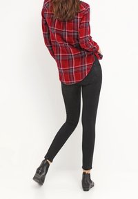 Red and black plaid shirt with button closure and rolled sleeves, paired with black skinny jeans and black ankle boots.