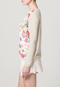 Kwiatowy sweter z białym przodem, ozdobiony kolorowymi kwiatami, z kremowymi, miękkimi rękawami i ściągaczem na dole. Prosty design z okrągłym dekoltem.