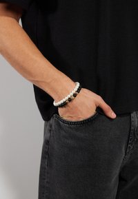 Svart og hvit perlesmykke, med perler og matte svarte perler, med et gullakent, båret på en håndleddet, kombinert med en mørk skjorte og jeans.