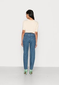 Camisa de manga curta bege clara, jeans de cintura alta azuis e sapatos de salto verdes. Tecido suave e corte reto com bolsos traseiros.