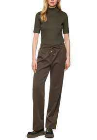 Olive green turtleneck top paired with dark brown tailored pants featuring a textured pattern and a drawstring waist. Black footwear with thick soles.