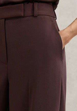 Tamnoplave krojene hlače glatke teksture, s bočnim džepom i petljom za remen oko struka. Čiste linije i klasični dizajn.