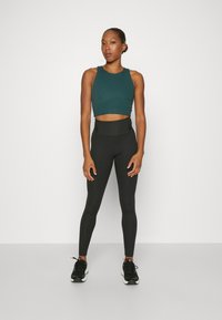 Teal rebrasti crop top u kombinaciji s crnim tajicama visokog struka. Crne atletske cipele zaokružuju odjevnu kombinaciju. Minimalistički dizajn, glatka tekstura.
