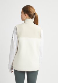 Ljusbeige fleeceväst med hög krage och en slät övre del, med en mjuk textur och rundade kanter.