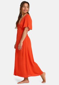 Vestito lungo arancione con maniche a svolazzare corte, scollo a V profondo e bottoni lungo la parte anteriore. Il tessuto ha un aspetto leggero e testurizzato.