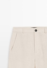 Pantalon beige clair avec passants de ceinture, poches latérales et fermeture par bouton noir à la taille sur fond blanc.