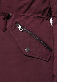 Burgunderjacka i tyg med texturerad finish. Har en sidodragkedjeficka, tryckknappdetalj och dragsko i midjan för justerbar passform.