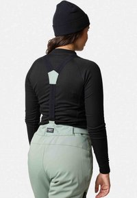 Black long-sleeve top with textured fabric, paired with light green pants featuring adjustable straps and a logo patch at the waist.