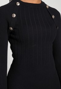 Robe en maille côtelée noire à manches longues, ornée de boutons argentés le long de l'épaule. Coupe ajustée avec une texture lisse.