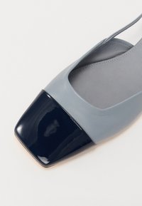 Chaussure en cuir bleu clair avec un bout carré, dotée d'un accent en cuir verni bleu marine au niveau du bout. Design plat et bride réglable à l'arrière.