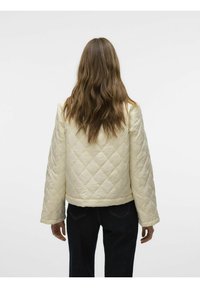 Chaqueta crema acolchada con un diseño cuadrado, que presenta mangas anchas y un dobladillo cortado. Textura suave con un patrón de costura en forma de rombo.