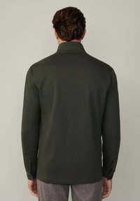 Camicia a maniche lunghe verde scuro con colletto, caratterizzata da una texture liscia e polsini con bottoni, vista dal retro.