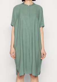 Zelené šaty s krátkým rukávem, kulatým výstřihem, zapínáním na knoflíky, volným střihem a bočními rozparky pro snadný pohyb. Měkká, lehká látka.