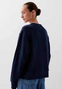 Felpa blu navy con maniche lunghe, scollo rotondo e vestibilità rilassata. Design minimalista con polsini e orlo a costine, realizzata in tessuto morbido.