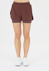 Braune sportliche Shorts mit einem elastischen Bund, die ein schichtiges Design und eine kurze Länge aufweisen. Kombiniert mit weißen Turnschuhen.