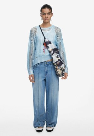 Pulover tricotat din plasă albastru deschis, cu croială lejeră, asortat cu blugi cu picioare largi. O geantă cu model este purtată transversal peste corp.