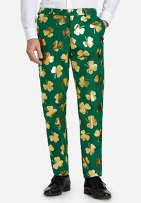 Zelene hlače z bleščečim zlatim clover vzorcem, prilegajoč dizajn in raven sprednji del; obute z črnimi čevlji in belim srajcem.