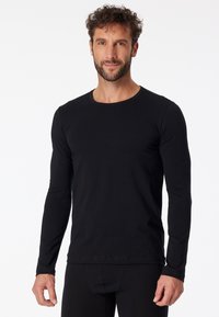 Camiseta de manga larga negra hecha de suave tela de algodón. Presenta un cuello redondo, mangas ajustadas y un diseño minimalista sin adornos.