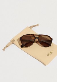 Sötét lencsés teknősmaszk napszemüveg bézs színű tokon, arany logóval. Állítható húzózsinóros záródás a tokon.