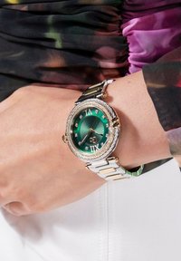 Roheline kell dial koos kuldsete aktsentidega, ümmargune korpus, teemantmarkerid ja kahes toonis metallist käevõru. Omab tekstureeritud päikesepaiste mustrit.