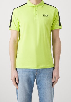 Polo vert citron vif avec des accents noirs sur les épaules, deux boutons sur le col, et un logo imprimé sur le côté gauche de la poitrine.