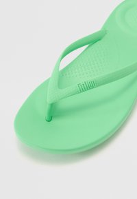 Roheline kummist plätu, millel on tekstuuriga jalapadi ja sile lõhkenud rihm. Rihmal on reljeefne logo, ümar tald.