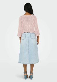 Pull en maille rose clair avec des manches 3/4 et un ourlet festonné, associé à une jupe midi en denim bleu et des sandales à talons.