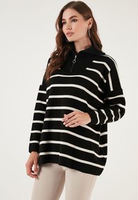 Pulover cu dungi alb-negru, cu guler cu fermoar la jumătate, croială lejeră și textură ribbed la guler și mansete. Material moale, casual.