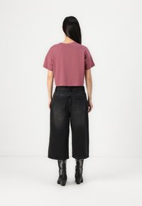 T-shirt curta de manga com um corte cropped na cor malva, combinada com uns jeans de ganga pretos, de perna larga e cintura alta. Botas pretas de salto e meias com padrões completam o visual.