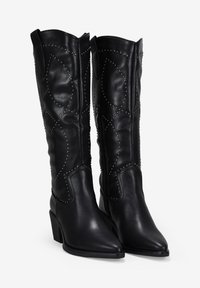 Botas altas de cuero negro, con punteras afiladas, que presentan detalles de tachuelas y un patrón texturizado de hojas a lo largo del eje. Tacones cuadrados gruesos.