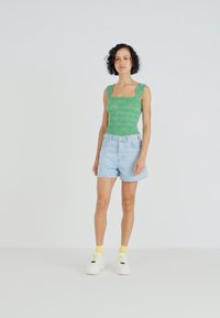 Zelen top s motivom, svetlo modre denim kratke hlače in bele superge z rumenimi nogavicami. Preprost dizajn, prilegajoča oblika, sproščen poletni outfit.