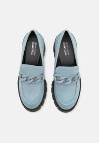 Blue denim loafers featuring a silver chain accent, a rounded toe, and a thick black rubber sole. Designed to be vegan-friendly.
