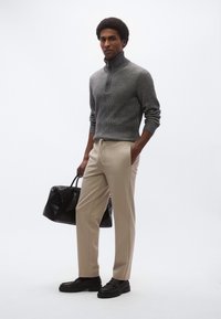 Maglione grigio a costine con mezza cerniera, pantaloni beige a gamba affusolata, borsa a sacco nera con trama e scarpe nere robuste. Design minimalista, vestibilità comoda.