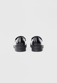 Scarpe di pelle nera con finitura lucida, tacco basso e impilato, forma arrotondata. Presentano un branding sottile sul tacco.