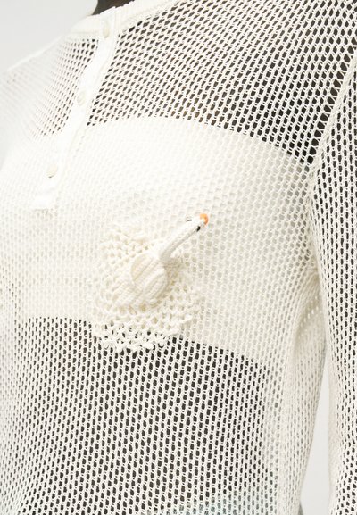 Chemise en maille résille blanche avec détail cygne crocheté en 3D sur la poitrine et encolure henley boutonnée.