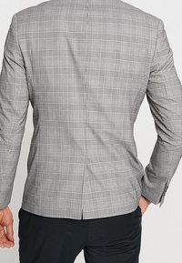 Grå rutigt kavaj med strukturerad passform, slagkrage, en slits bak, och knäppte ärmar med en mjuk textur.