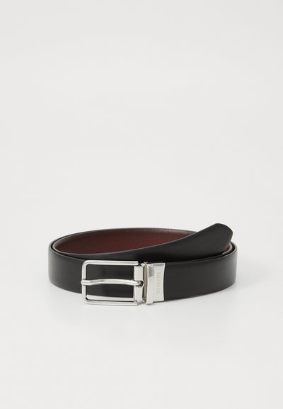 Zwarte leren riem met een zilveren rechthoekige gesp, die een glad oppervlak en een contrasterende rode binnenvoering toont, ligt plat op een witte achtergrond.