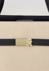 Beige geweven stoffen toilettas met zwarte leren accenten en een gouden decoratieve sluiting met een logo. Glad oppervlak en gestructureerde vorm.