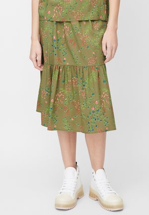 Jupe midi fleurie verte avec ourlet volanté à étages portée avec des baskets blanches montantes sur une personne debout.