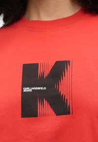 Czerwona bawełniana koszulka z czarnym nadrukiem przedstawiającym literę "K" oraz napis "Karl Lagerfeld Jeans". Krótkie rękawy i okrągły dekolt.