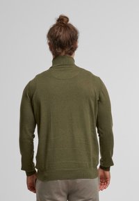 Olivgrüner Rollkragenpullover aus weichem Strickmaterial. Verfügt über gerippte Ärmelbündchen und Saum, eine eng anliegende Silhouette und ein nahtloses Schulterdesign.