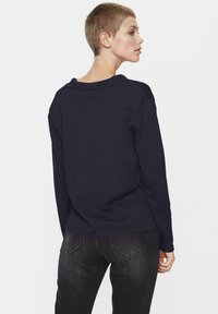 Navy long-sleeve top with a rounded collar and a relaxed fit, paired with dark gray fitted jeans, displaying smooth fabric texture.