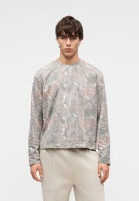 Μπλούζα με μακριά μανίκια σε διακριτικό, μοτίβο καμουφλάζ με αποχρώσεις του γκρι και καφέ. Απαλή υφή, στρογγυλή λαιμόκοψη και άνετη εφαρμογή.