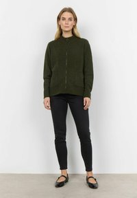 Olivgrön zip-up kofta med krage, två framfickor, stickad textur och avslappnad passform, i kombination med svarta byxor och ballerina.