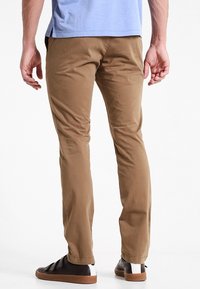 Chino in cotone color caramello con taglio slim, caratterizzati da una texture liscia e dettagli di cucitura sottili, abbinati a sneaker marroni con inserto slip-on.
