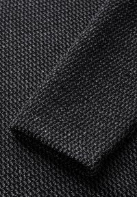 Schwarzer Strickstoff mit einem strukturierten Muster. Die Oberfläche besteht aus kleinen, erhabenen geometrischen Formen, die eine taktile Qualität verleihen.
