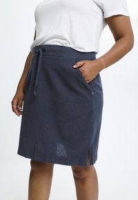 Jupe en lin bleu marine avec taille à cordon, poches latérales et légers fentes latérales. Présente une coupe décontractée et une texture lisse.
